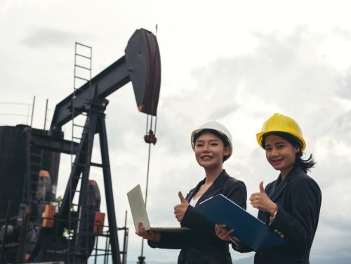 two-female-engineers-stand-beside-working-oil-pumps-with-white-sky